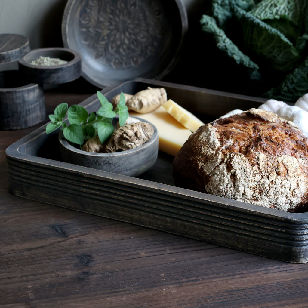 distressed black wooden serving tray displayed with bread and cheese sat on a wooden table