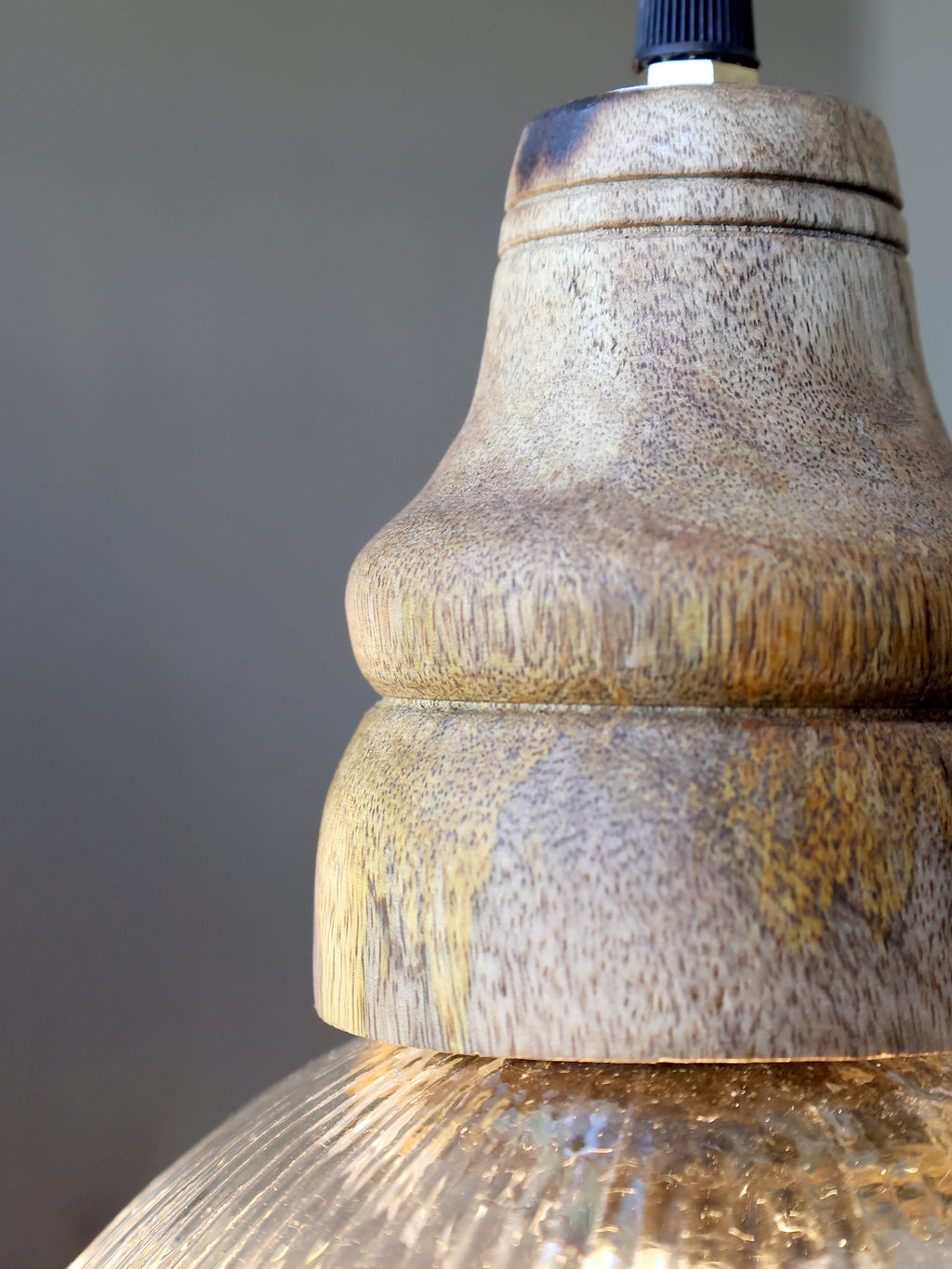 close-up wooden top of fluted glass pendant light against grey wall