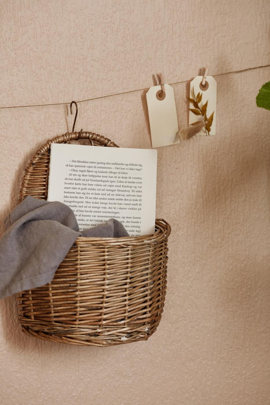 willow wicker small hanging basket storing accessories displayed hanging from a hook against a dusky pink wall